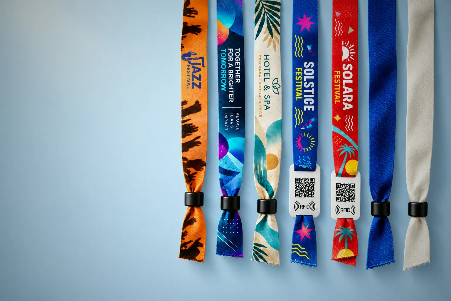 Printed fabric festival wristbands and RFID wristbands from JM Band hanging side by side against a light blue background